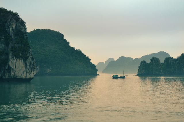 Boat sailing through tranquil waters amid towering limestone islands at sunset. Ideal for travel brochures, adventure blogs, nature magazines, and promotional material for serene and scenic destination spots.