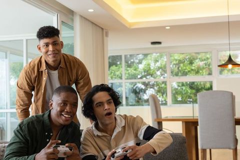 Diverse friends playing video games on couch in modern sunlit apartment lounge