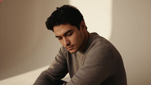 Man leaning and gazing downward in warm beige portrait wearing ribbed knit sweater