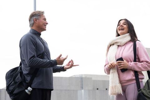Smiling workout partners chatting and laughing on urban rooftop with gym bags