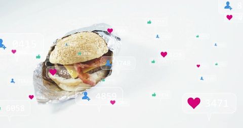 Sesame Burger Wrapped in Foil Resting on White Table with Floating Social Media Likes