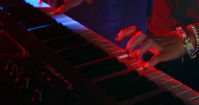 Person skillfully playing keyboard in a dimly lit music studio with red lighting. Ideal for content related to music production, performance, electronic instruments, and musical practice sessions.