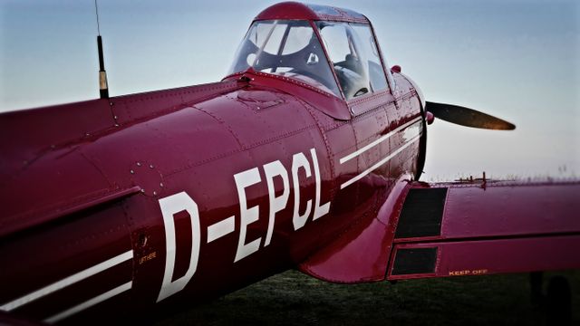 This vintage red airplane with D-EPLC markings is parked on grass, showcasing its classic design and reflecting the history of aviation. Perfect for use in topics related to aviation history, historic planes, retro transportation, air travel stories, or nostalgic themes.