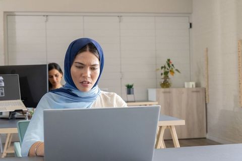 Woman in blue headscarf working on laptop in modern shared coworking office space