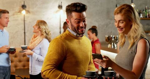 Friends Laughing and Using Mobile Phone in Coffee Shop