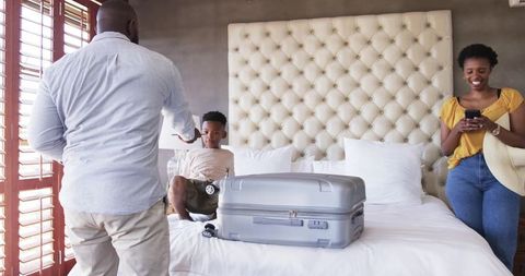 African american family packing suitcase on bed in hotel room with tufted headboard