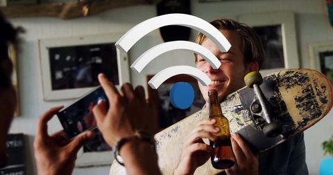 Man Holding Skateboard with Beer Smiling, Filmed by Friend Indoors
