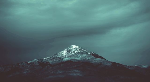 Snow-capped mountain peak under dramatic and cloudy sky. Ideal for use in travel promotions, nature documentaries, desktop wallpapers, outdoor adventure marketing, and winter-themed content.