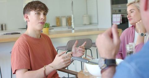 Teenager talking with family around modern kitchen island over casual shared meal