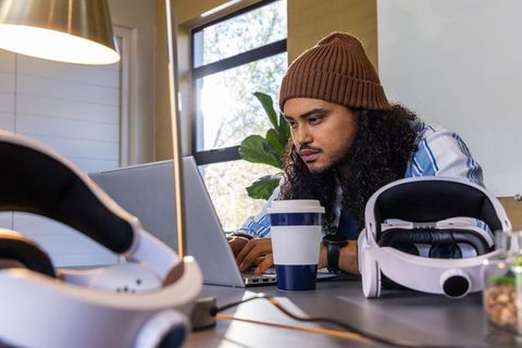 Working from home developer using laptop with vr headsets on desk and coffee cup
