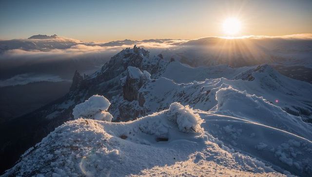 Sunrise bathing snowy alpine ridge with sculpted cornices and backlit peaks above cloud inversion