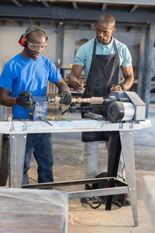 African american instructor guiding teen turning wood lathe hands-on woodworking workshop