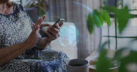 Senior woman tapping smartphone while browsing apps with holographic globe overlay