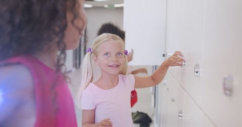 Joyful schoolgirls using lockers in school hallway