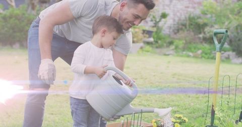 Father teaching son watering flowers with large watering can in sunny backyard