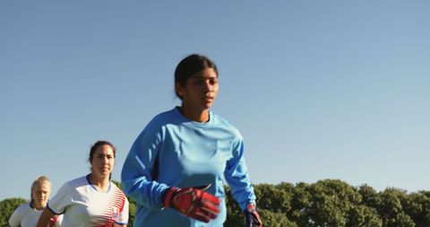 group of diverse female soccer players running on a sunny field, exemplifying teamwork and athleticism. suitable for depicting women in sports, promoting diversity in athletics, or illustrating active and healthy lifestyles. can be used in content related to women's empowerment in sports, team dynamics, or as a visual for advertisements about football training gear.