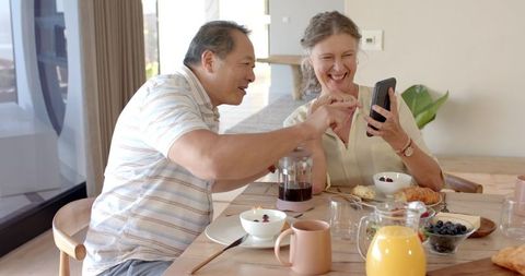 Senior couple enjoying breakfast together using smartphone