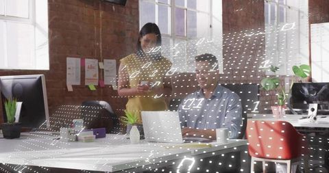 Smiling coworkers collaborating over laptop in modern industrial office with data overlay