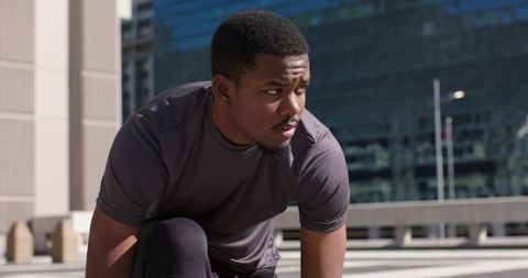 Urban African American athlete preparing to sprint on rooftop with city skyline