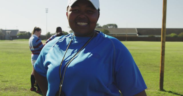 Portrait of happy african american female rugby trainer wearing cap with arms crossed on field. Sport, rugby, active lifestyle and competition concept, unaltered.