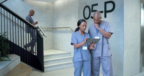 African american medical team reviewing tablet in hospital corridor near staircase
