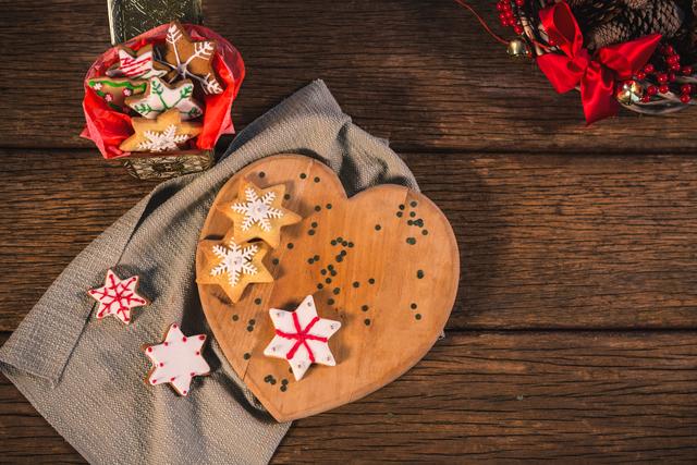 Scene of Christmas gingerbread cookies with colorful icing on wooden table. Cookies shaped like stars and placed on heart-shaped wooden board. Suitable for holiday recipes, festive greeting cards, seasonal decorations, and food blog posts.