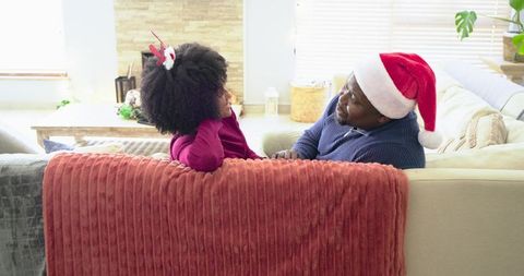 African American father and child sharing cozy holiday moment on sofa wearing Santa hat