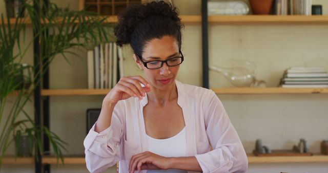 Businesswoman working at home office desk, wearing glasses, appearing focused on task at hand. Ideal for representing remote work, productivity, professional working environments, and modern working women. Can be used in articles about remote work, home office setups, productivity tips, business consultation, or professional lifestyle.