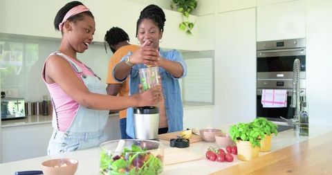 African family cooking together in modern kitchen blending green smoothie and making salad