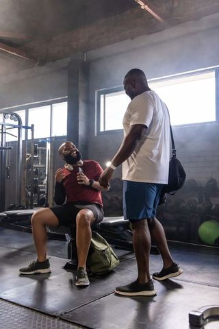 African american fitness partners trading fist-bump on weight bench in industrial gym