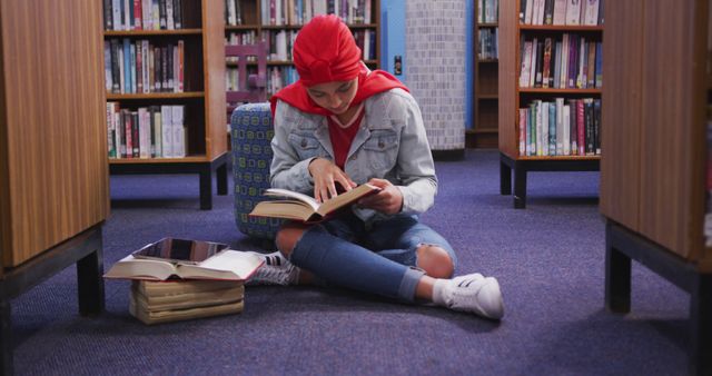 Teenage Biracial girl engrossed in reading at the library. She's surrounded by books, creating a peaceful study environment at school.