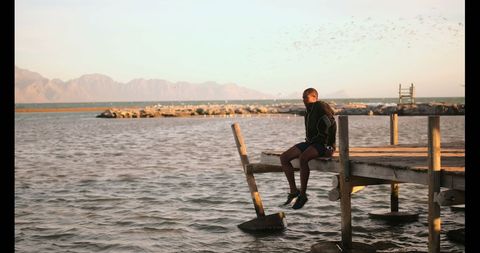Young Runner Relaxing on Pier Overlooking Serene Beachscape