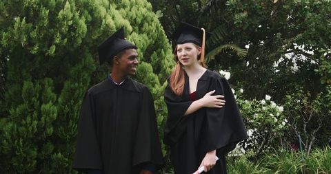 Diverse graduates celebrating on campus lawn wearing caps and gowns holding diplomas