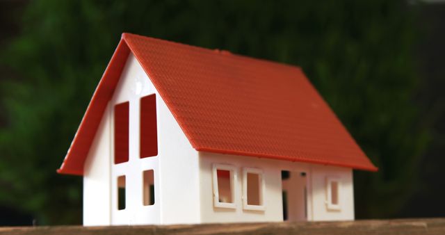A small model of a house with a red roof is displayed, symbolizing real estate and property ownership concepts. Its simplicity and the green background suggest a focus on the idea of home and investment opportunities.
