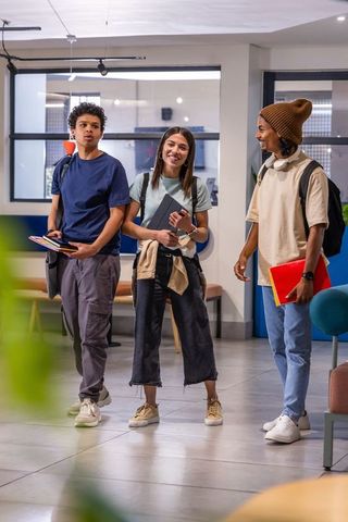 Multiracial students chatting in modern campus lounge with backpacks and tablets