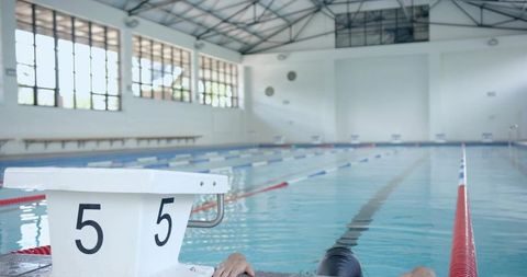 Male swimmer exiting pool with numbered block in large indoor facility