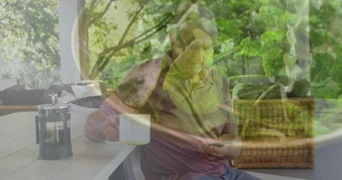 Senior Man Relaxing on Sunlit Porch Holding Coffee and Smartphone Among Lush Greenery