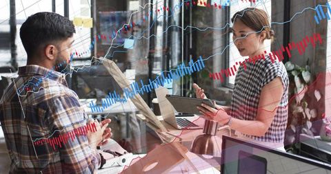 Colleagues discussing data analytics and charts with laptop and tablet in modern office