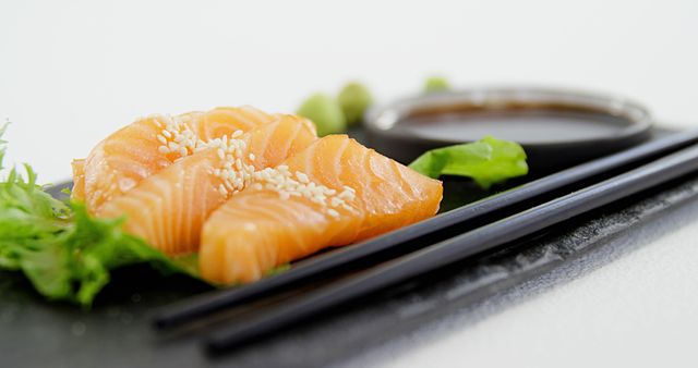 Slices of fresh salmon sashimi with sesame seeds on top, accompanied by soy sauce and green leaf garnish. Perfect for illustrating high-quality dining, Japanese cuisine, restaurant menus, food blogs, and healthy eating concepts.