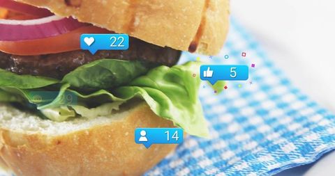 Closeup gourmet burger showing social media notifications overlaid on blue checkered cloth