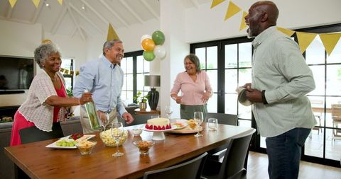 Joyful Senior Friends Preparing Birthday Party Table in Warm Home