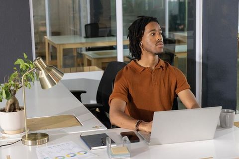 Young professional working on laptop in modern open-plan office reviewing business charts