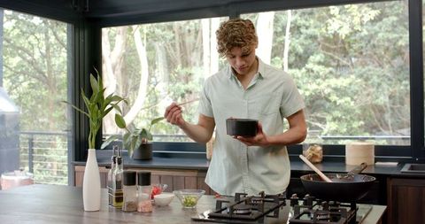 Young Man Cooking Soup in Modern Kitchen with Greenery View