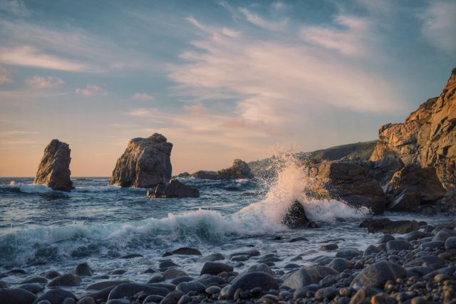 Depicts waves crashing on a rocky pebble beach with dramatic sky during sunset. Ideal for websites, blogs, and advertisements promoting travel, nature, relaxation, and coastal tourism.