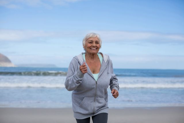 Senior woman jogging on the beach, smiling and enjoying her exercise routine. Ideal for promoting active lifestyles, fitness programs for seniors, healthy living, and wellness campaigns. Perfect for illustrating outdoor activities, retirement life, and the benefits of staying active in older age.
