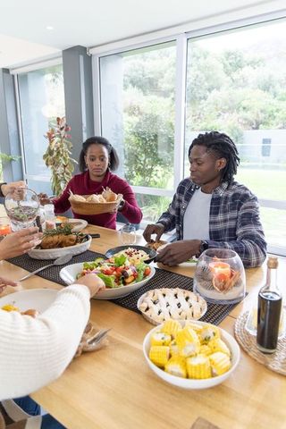 African american couple sharing family meal at modern dining table with roasted chicken, salad and c