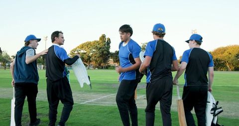 Young amateur cricket team gathering on pitch preparing for match in sunlit park field