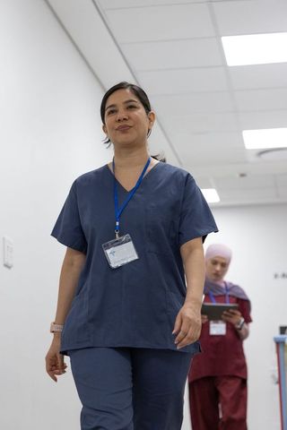Diverse female nurses walking clinic corridor in navy and maroon scrubs wearing id badges