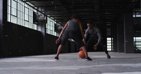 Man dribbling and woman defending during urban basketball training in industrial warehouse