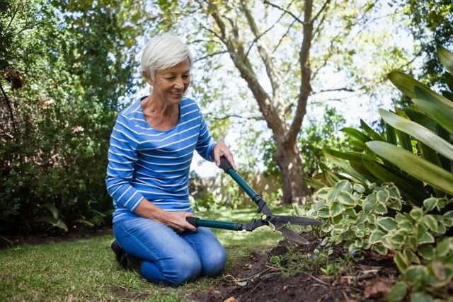 Senior woman kneeling while cutting plants with hedge trimmer at backyard